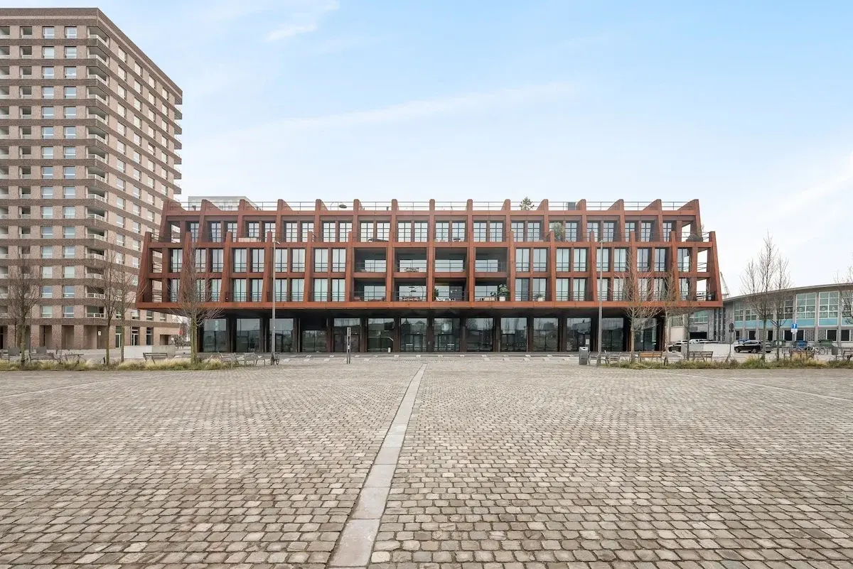 Edificio moderno con fachada de acero color óxido junto a una plaza adoquinada